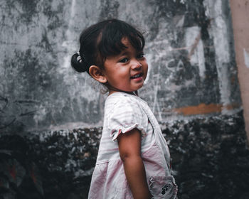 Cute girl looking away while standing against wall