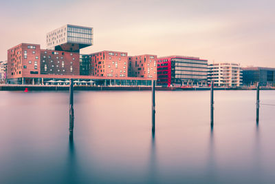Buildings by spree river against sky during sunset
