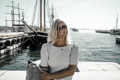 Portrait of smiling woman sitting by sea against sky