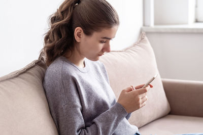 Side view of girl using mobile phone while sitting on sofa at home