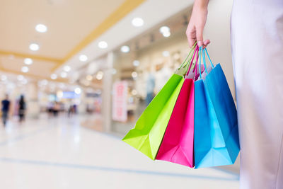 Midsection of woman holding colorful shopping bags at mall