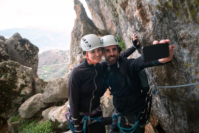 Concept: adventure. pair of climbers with helmet and harness. taking a selfie with the smart phone. at the top of the mountain. via ferrata in rock.