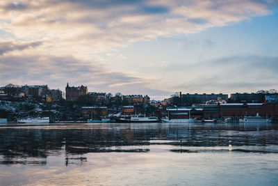 River by buildings against sky during sunset in city