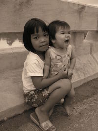 Portrait of smiling girl with brother sitting against railing 