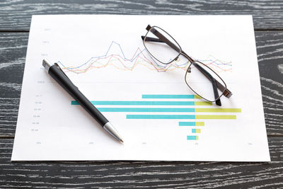 Close-up of pen and eyeglasses with graphs on table at office