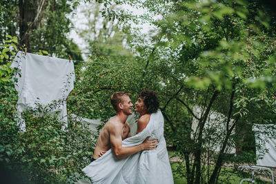 Young couple standing by plants against trees