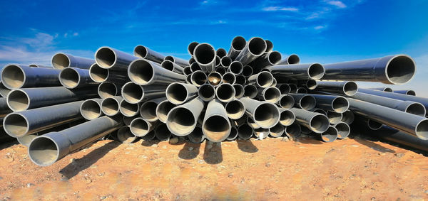 Stack of pipes on field against sky