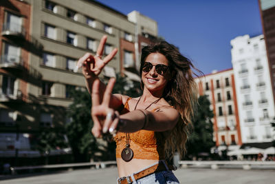 Portrait of young woman gesturing while standing in city