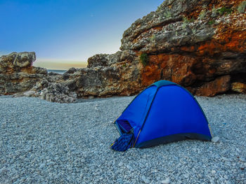 Tent on rock by sea against blue sky