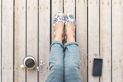 Low section of woman with coffee and mobile phone sitting on wood