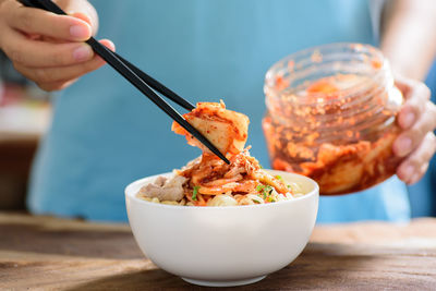 Midsection of woman using chopsticks while picking food from bowl on table