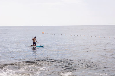 Man with a beard swims on stand up paddle board on a quiet blue ocean. sup surfing in water