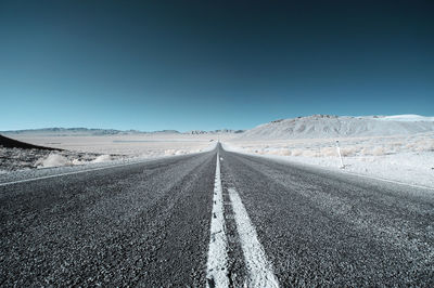 Road on snow covered landscape against clear sky