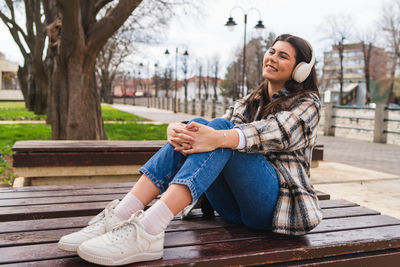 Young woman using mobile phone while sitting on bench at park