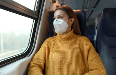 Young woman wearing mask looking out of train window