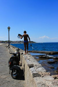 Rear view of man standing on sea against clear sky