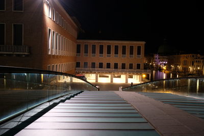 Footpath by illuminated buildings in city at night