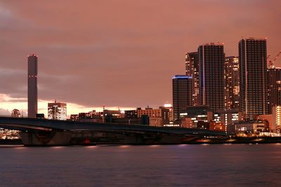 River and illuminated city against sky during sunset