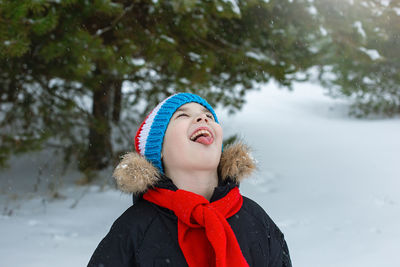 Funny boy in winter clothes and a red scarf catches snowflakes with his tongue