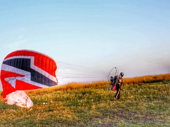 Man with powered parachute on grassy field against clear sky during sunset
