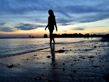 Silhouette girl walking on beach against sky during sunset