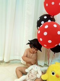 Girl holding balloons while standing by curtain at home