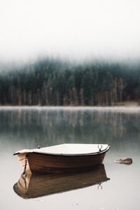 Boat moored on lake against trees during foggy weather