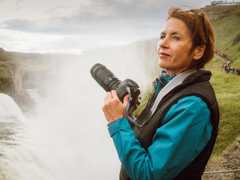 Side view of woman photographing against waterfall