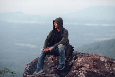 Side view of woman sitting on rock against sky