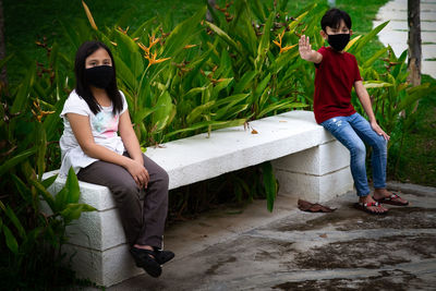 Two asian children wearing mask sitting in distance of 1 meter from others keeping distancing. 