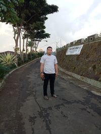 Full length portrait of young man standing against trees