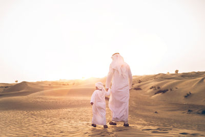 Rear view of friends walking on sand dune against sky