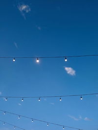 Low angle view of birds perching on cable against blue sky