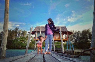 Full length portrait of mother and daughter against sky