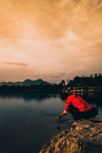 Woman sitting on lake against sky during sunset