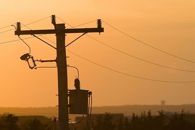Low angle view of silhouette electricity pylon against sky during sunset