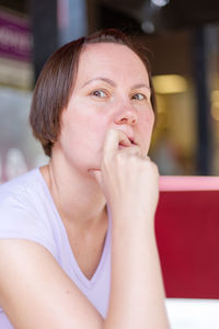 Portrait of young woman with finger in mouth sitting at cafe