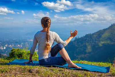 Side view of woman sitting on mountain against sky