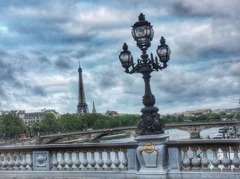 Low angle view of bridge and buildings against cloudy sky