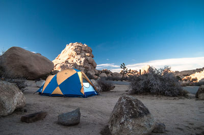 Tent field by rocks against blue sky