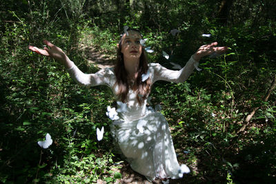 Butterflies flying over woman sitting with arms raised at forest