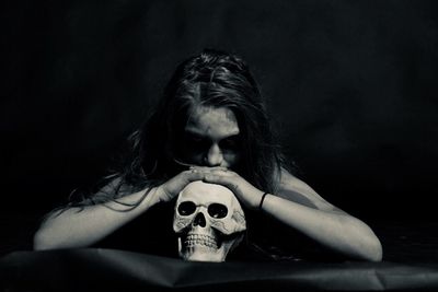 Woman leaning on human skull against black background