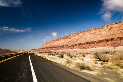 Country road leading towards mountains against blue sky