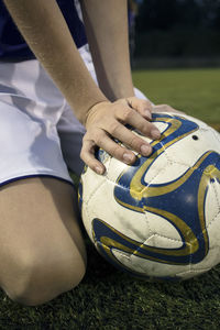 Midsection of girl kneeling by soccer ball on field