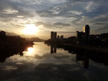 Reflection of silhouette buildings in lake against sky during sunset