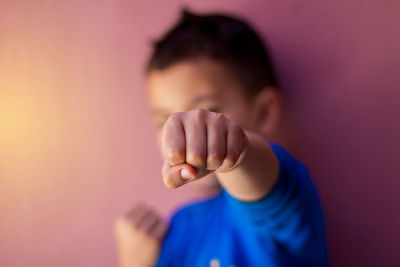 Close-up of boy showing fist while standing by wall