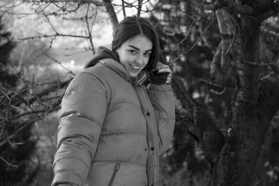 Portrait in black and white of smiling young woman standing against trees during winter 