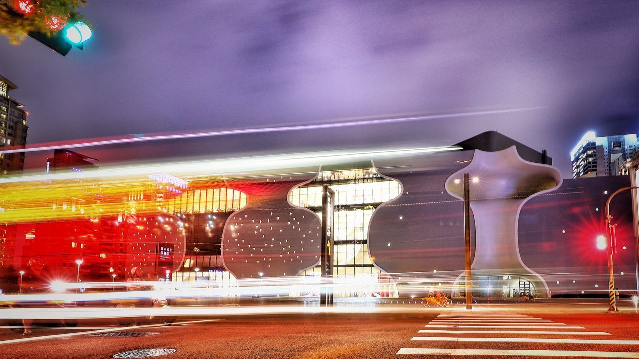 LIGHT TRAILS ON ROAD AGAINST BUILDINGS AT NIGHT