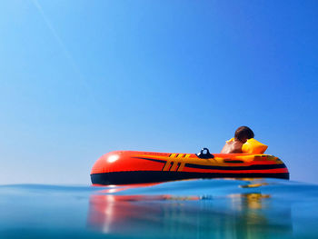 Yellow toy floating on water against clear blue sky