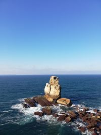 Rocks in sea against clear blue sky